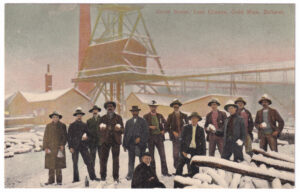 A postcard with a photo of a group of men gathered in front of a gold mine (with the area covered in snow).